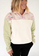 A woman wearing a Simply Southern quarter-zip fleece pullover with a cream body, light green sleeves, and a pink-and-white floral patterned yoke, paired with black pants against a white studio background.