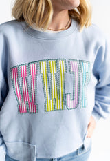 Close up of women's WWJD striped patch lettering on light blue crewneck faith graphic sweatshirt

