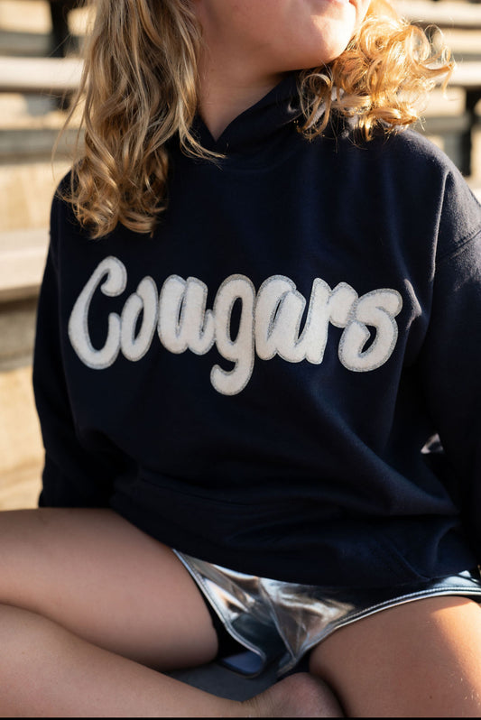 Absolutely! Here’s a Shopify description for the youth version of the navy Cougar hoodie in sizes S–L:

---

**Youth Cougar Spirit Hoodie – Navy Fleece**
Let your little Cougar fan cozy up in team pride! This youth-sized navy hoodie is soft, sporty, and full of school spirit—perfect for chilly bleachers, spirit week, or just repping their favorite team with big kid energy.

🐾 **Details:**

* Navy pullover with soft fleece lining
* White chenille *Cougars* patch across the chest
* Classic kangaroo pocket 