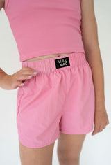 Girl wearing pink shorts with the branding Lulu Mac on a black label