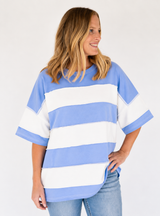 A woman wearing an oversized short-sleeve t-shirt with wide horizontal light blue and white stripes, paired with light-wash blue jeans, photographed against a plain white studio background.