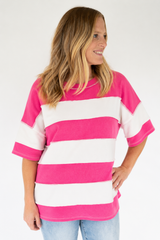 A woman wearing a bright pink and white horizontally striped short-sleeve t-shirt, paired with light blue jeans, photographed against a solid white studio background.