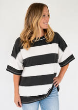 A woman wearing a black and white horizontally striped short-sleeve t-shirt with light blue jeans, photographed against a plain white studio background.