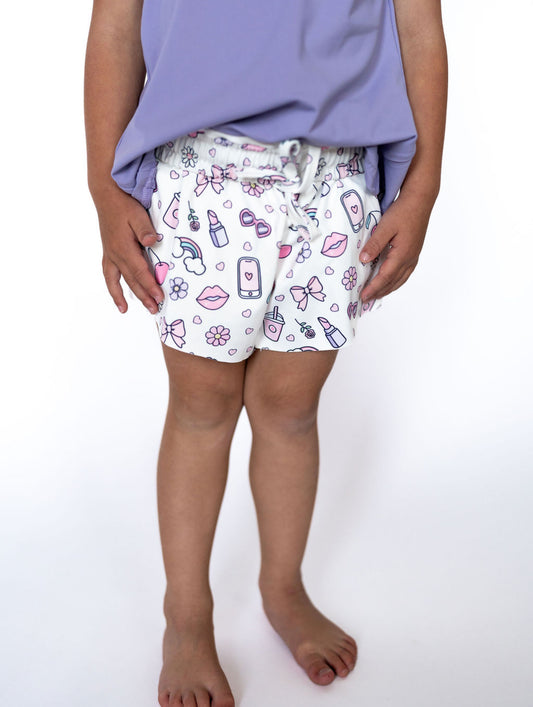These playful printed shorts are a whole&nbsp;mood – featuring fun little doodles of sunnies, lip gloss, phones, milkshakes, and more! Perfect for twirling, lounging, or strutting their stuff in style. Smaller fitted shorts on the inside.&nbsp;
Made with soft, lightweight fabric for all-day comfort

Elastic waistband with a cute bow tie detail

Whimsical pastel icons for the ultimate girly vibe

Easy pull-on design for quick outfit changes

