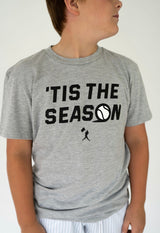 Boy wearing a gray tee shirt that says " Tis the Season" with a baseball and a baseball player graphic