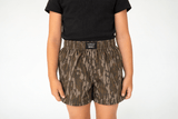 Lulu Mac Youth Mossy Oak Bottomland boxer short in a camouflage print with an elastic waistband and black Lulu Mac logo patch at the waist.